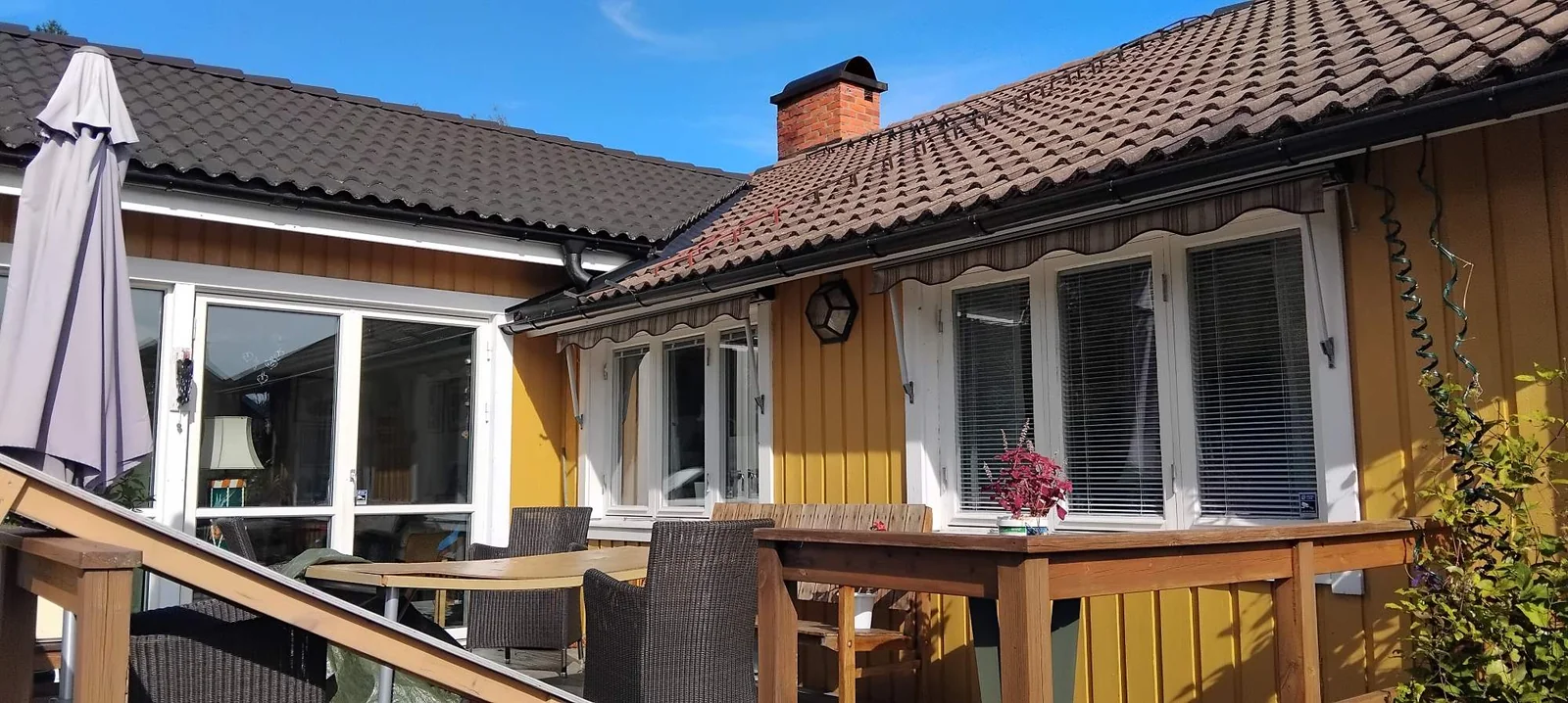 Gult trähus med terrass och ett mörkt tegeltak med påväxt